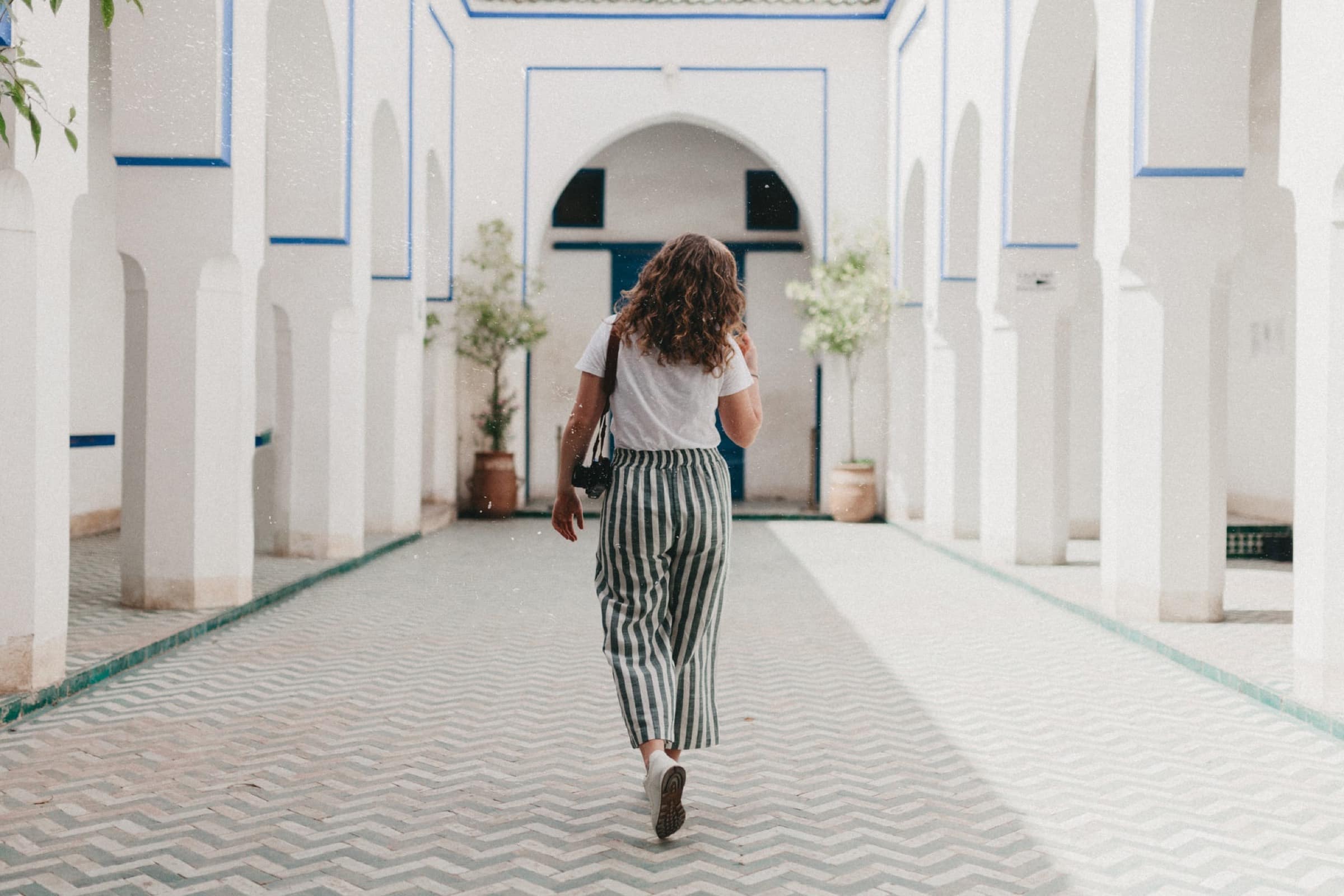 Une voyageuse traverse le patio d'un riad en tenue claire et légère, baskets aux pieds